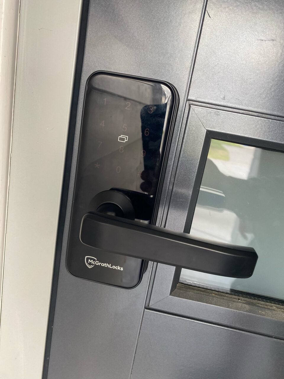 Black smart lock and lever handle installed on a dark glazed door by Bay Locksmiths