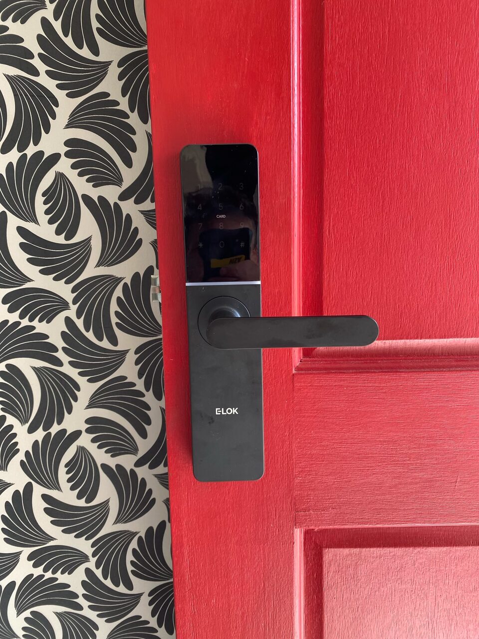 Black smart lock and lever handle installed on a red panelled door by Bay Locksmiths